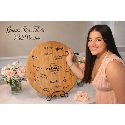Wedding guest signing personalized wooden wine barrel head guestbook with well wishes for the bride and groom at a wedding reception.
