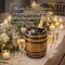 Rustic oak barrel wine and champagne chiller with bottle on ice surrounded by candles and floral arrangements at elegant wedding reception table